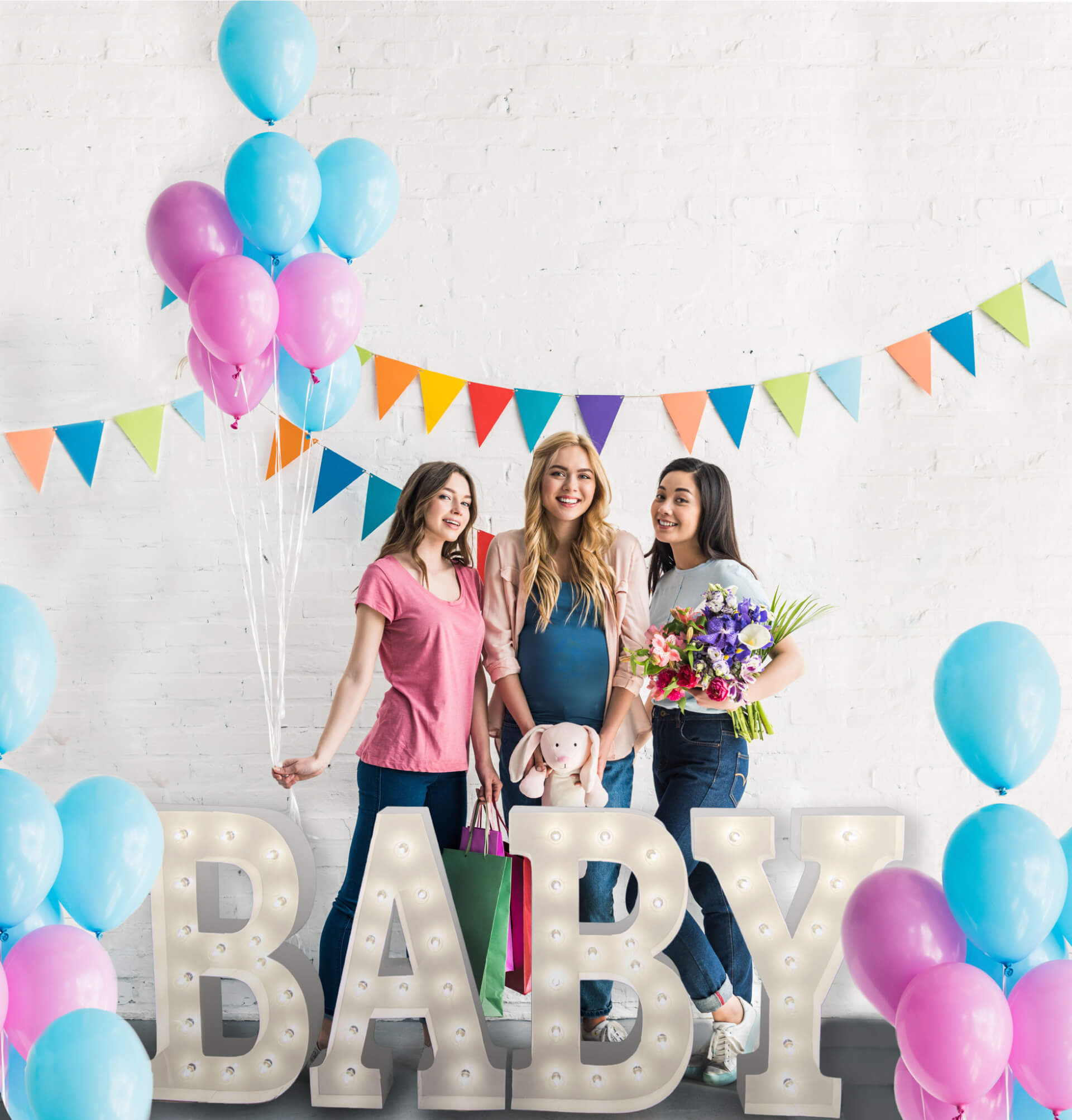 Three young women celebrating at a baby shower with the word "Baby" in marquee letters