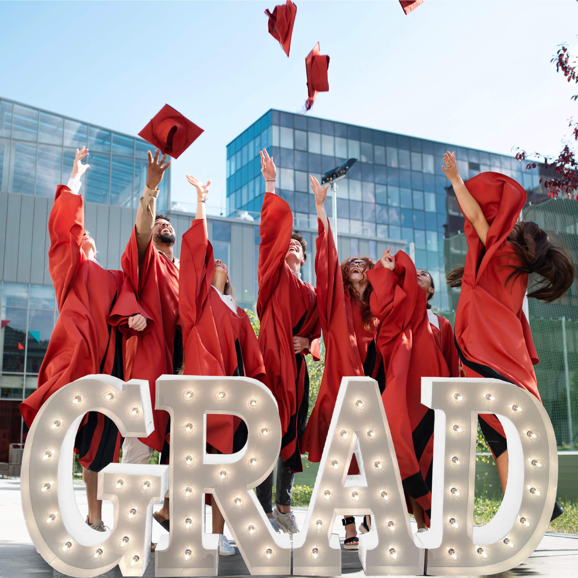 Young adults celebrating their graduation, throwing caps into the air with the word "Grad" in marquee letters