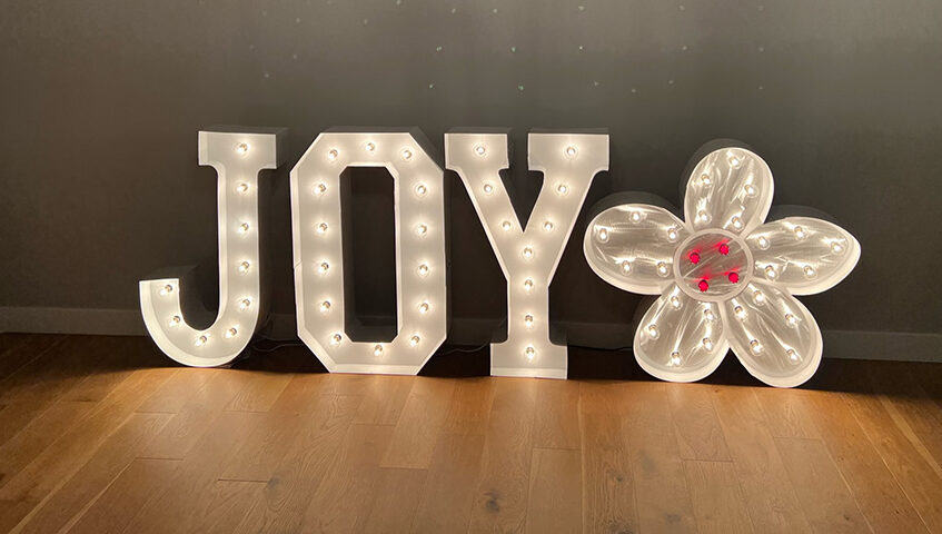 JOY in lit marquee letters with Flower in lit marquee letters