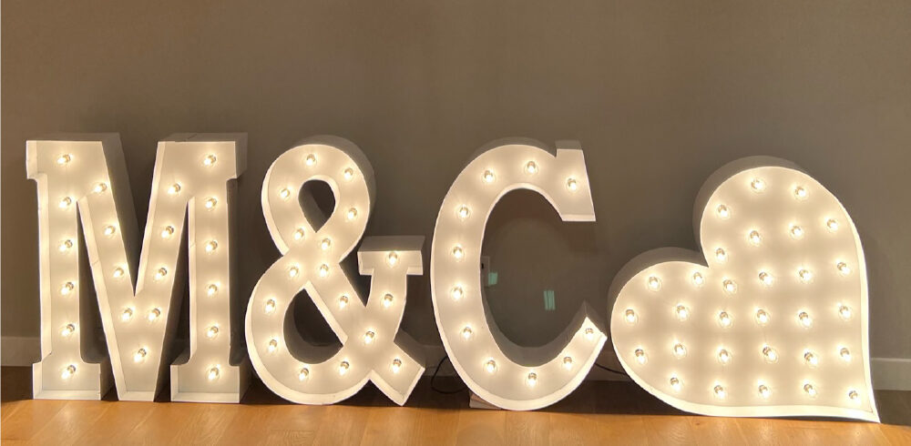 'M&C' in lit marquee letters with a lit marquee heart