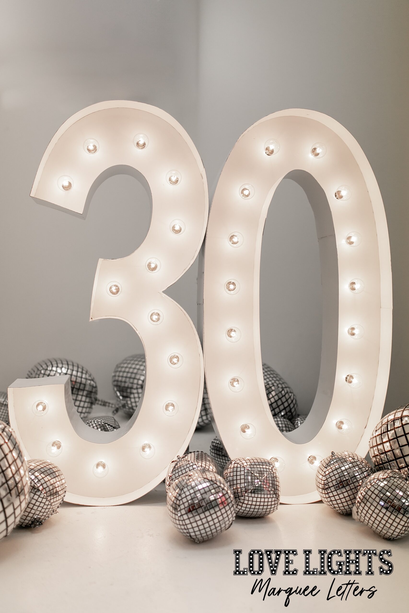 30 in lit marquee letters in a room with balloons
