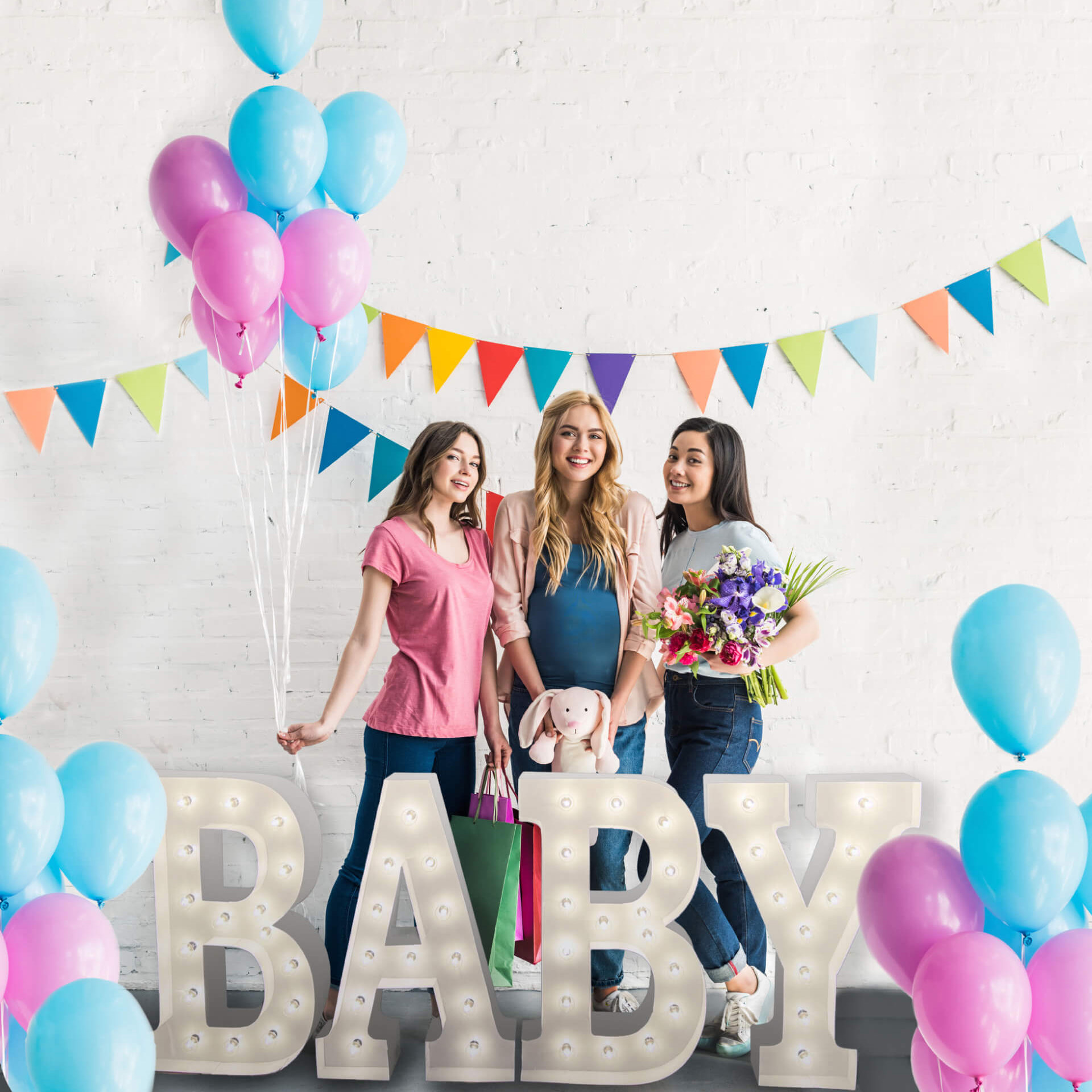 Three young women celebrating at a baby shower with the word 'Baby' in marquee letters