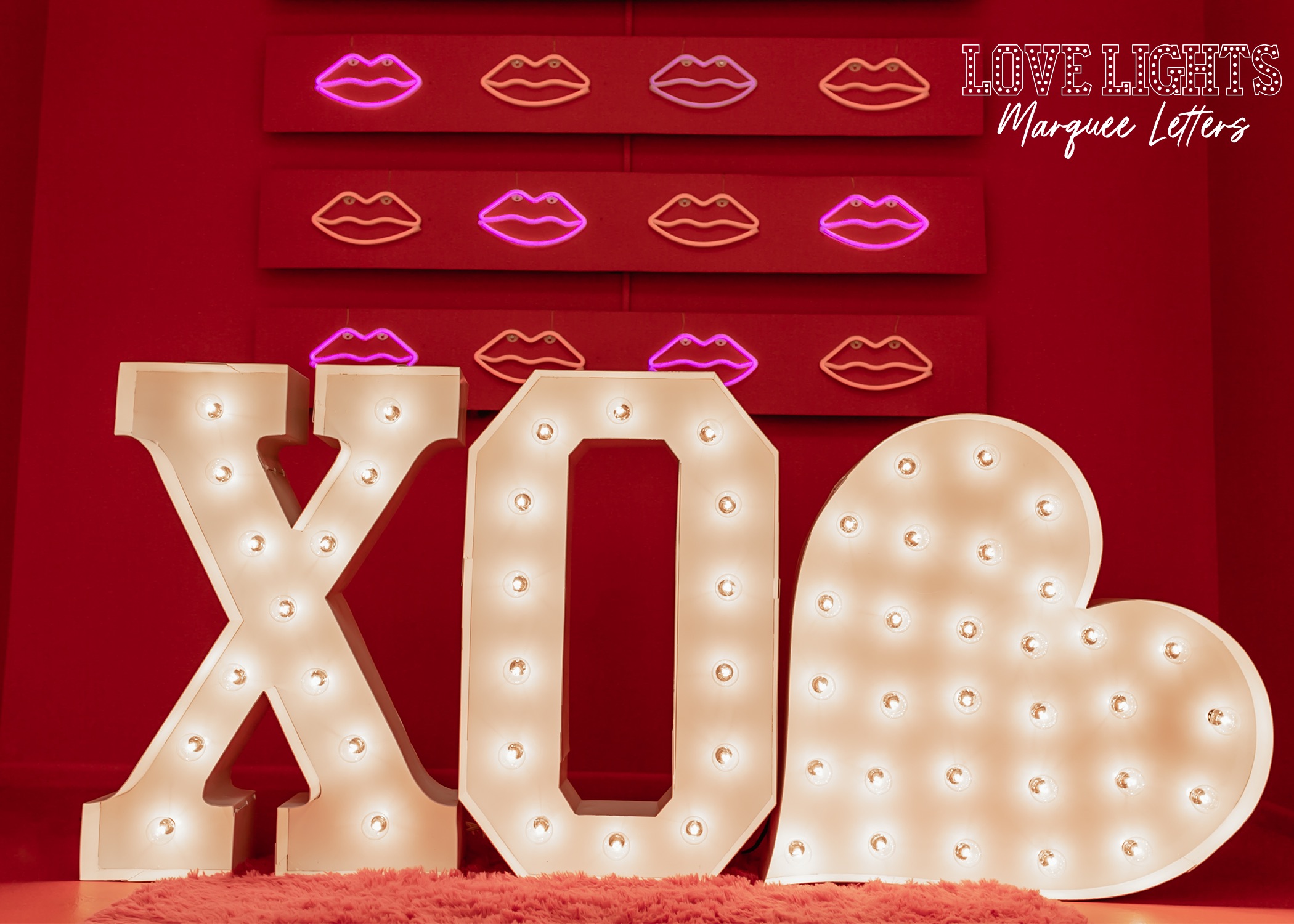 XO in lit marquee letters with a heart in lit marquee letters in a red room with LED lip lights behind