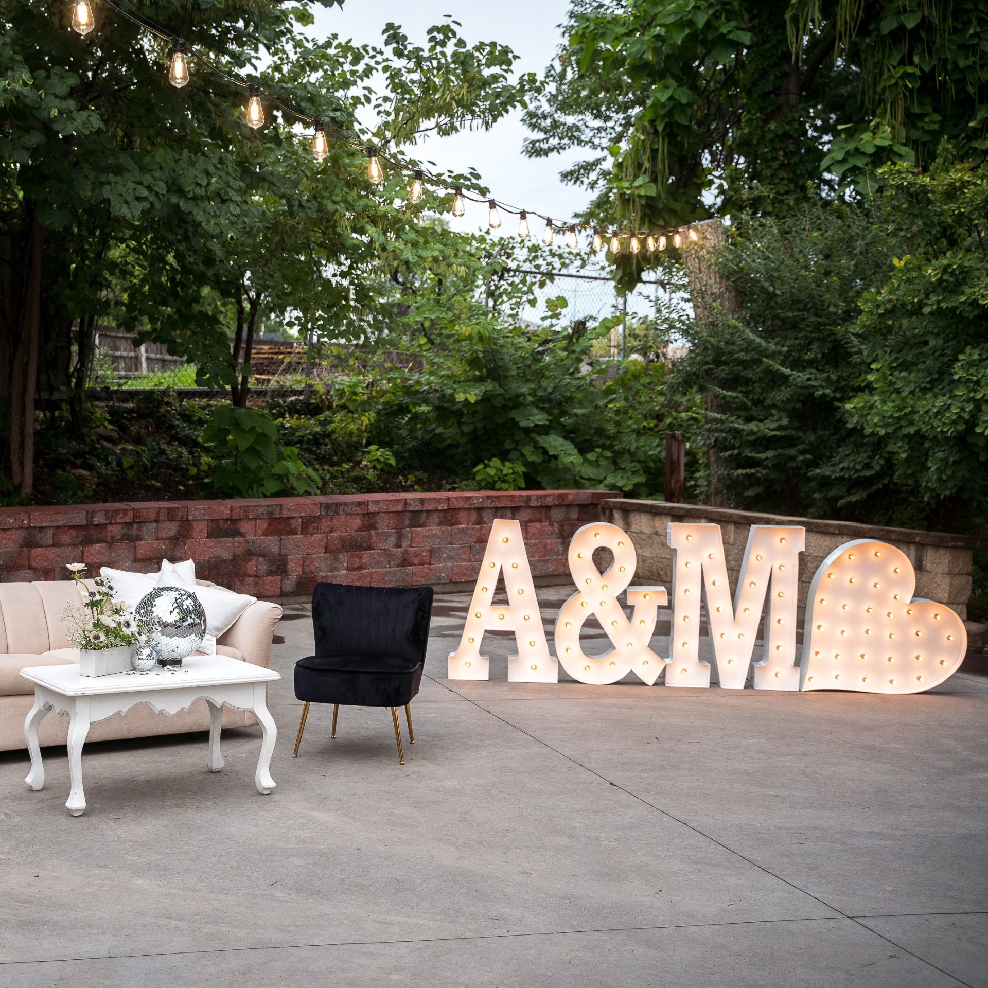 Big light up marquee letters A&M with a heart outside on a patio with black and white furniture staged for Love Lights