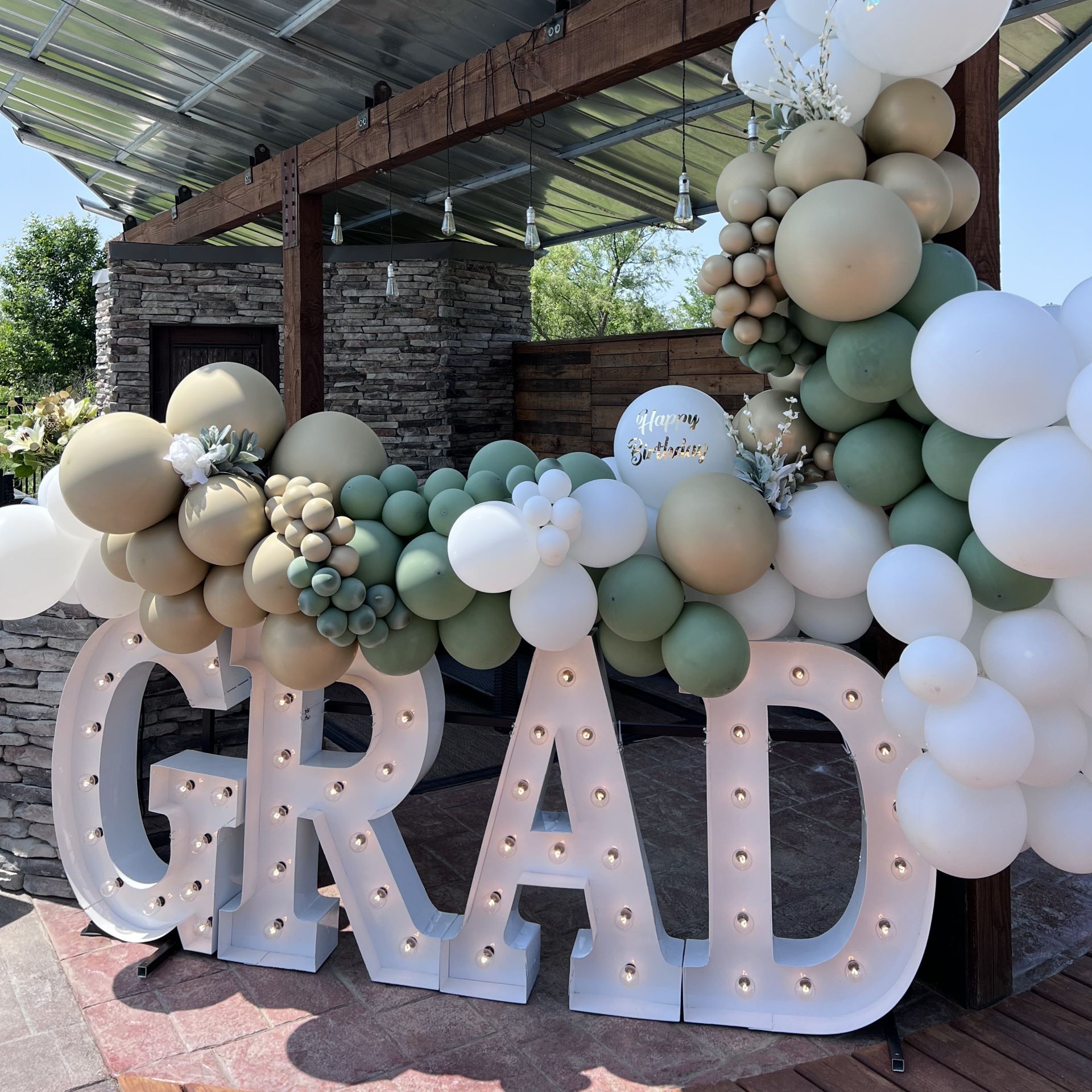 GRAD Marquee Lights with Sage green, white, and gold balloons at an event venue
