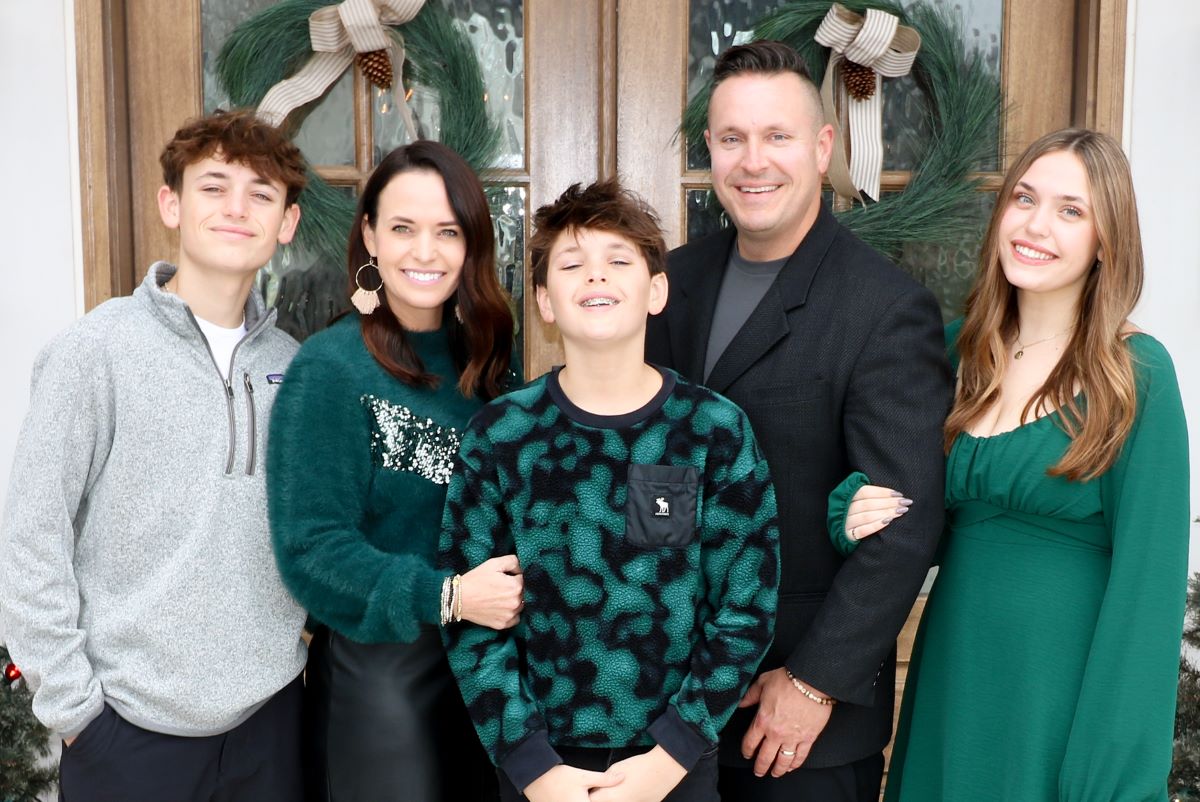 The Briley family - Mom, Dad, Girl & 2 boys - smiling in front of their front door - Christmastime - dressed in shades of green